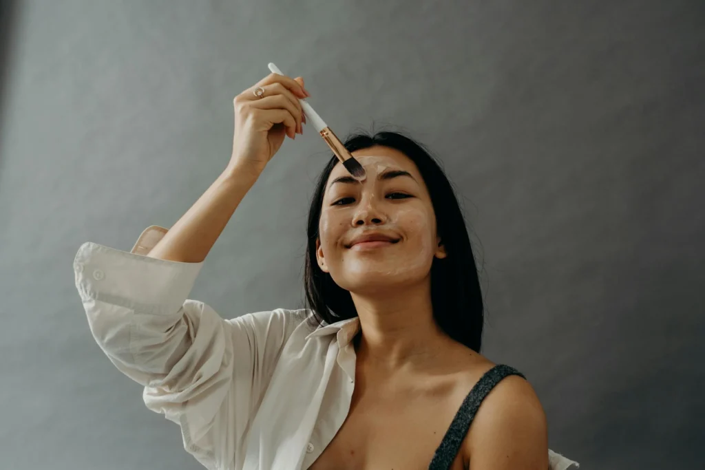 Eine lächelnde Frau trägt eine Gesichtsmaske auf, symbolisiert die Vorteile des Hydrafacials für eine strahlende und gesunde Haut