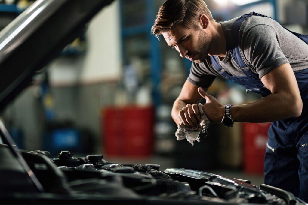 Junger Automechaniker, der sich die Hände putzt, nachdem er in einer Garage am Automotor gearbeitet hat.