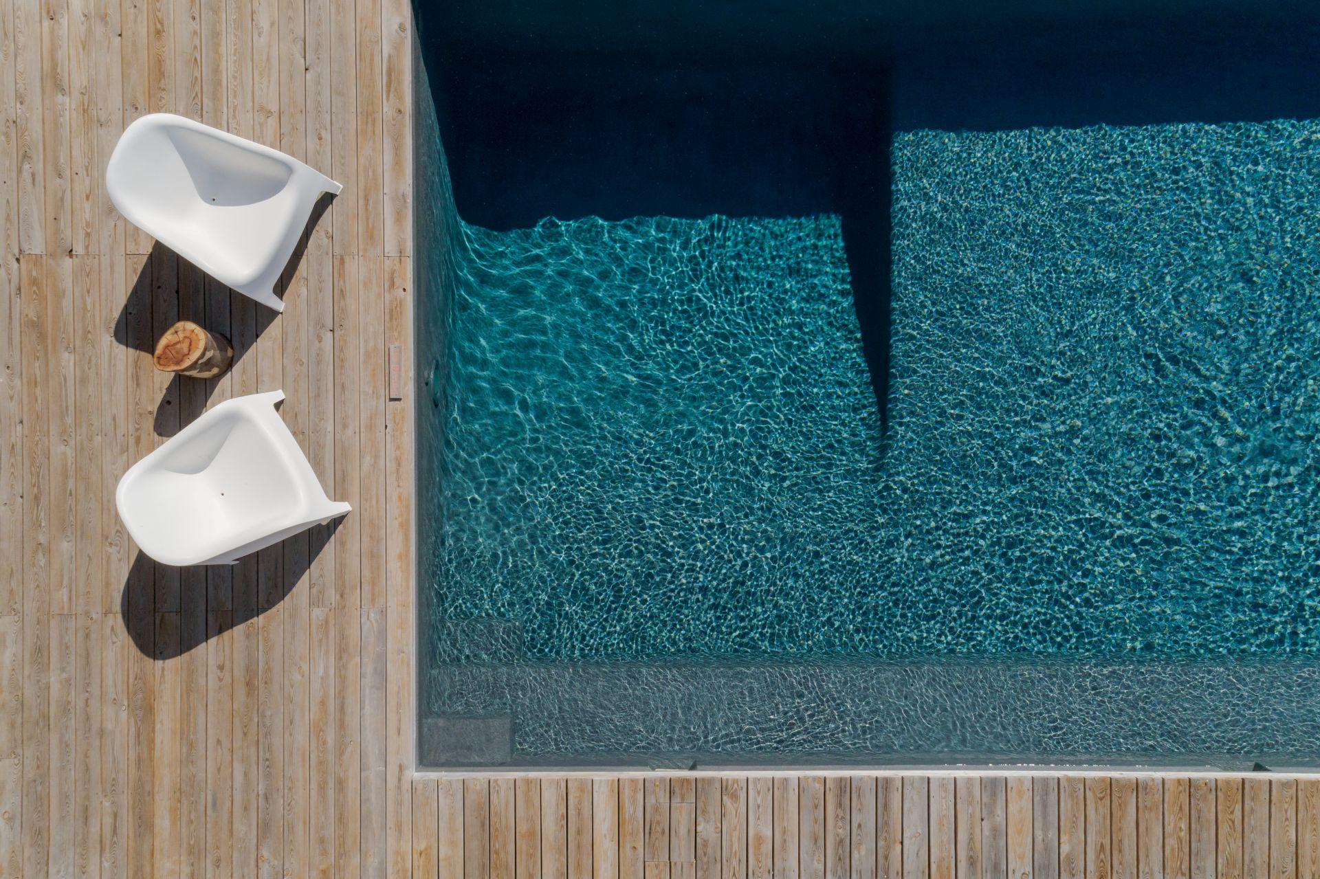 Luftaufnahme eines minimalistischen Pools mit Holzdeck und zwei weissen Sesseln