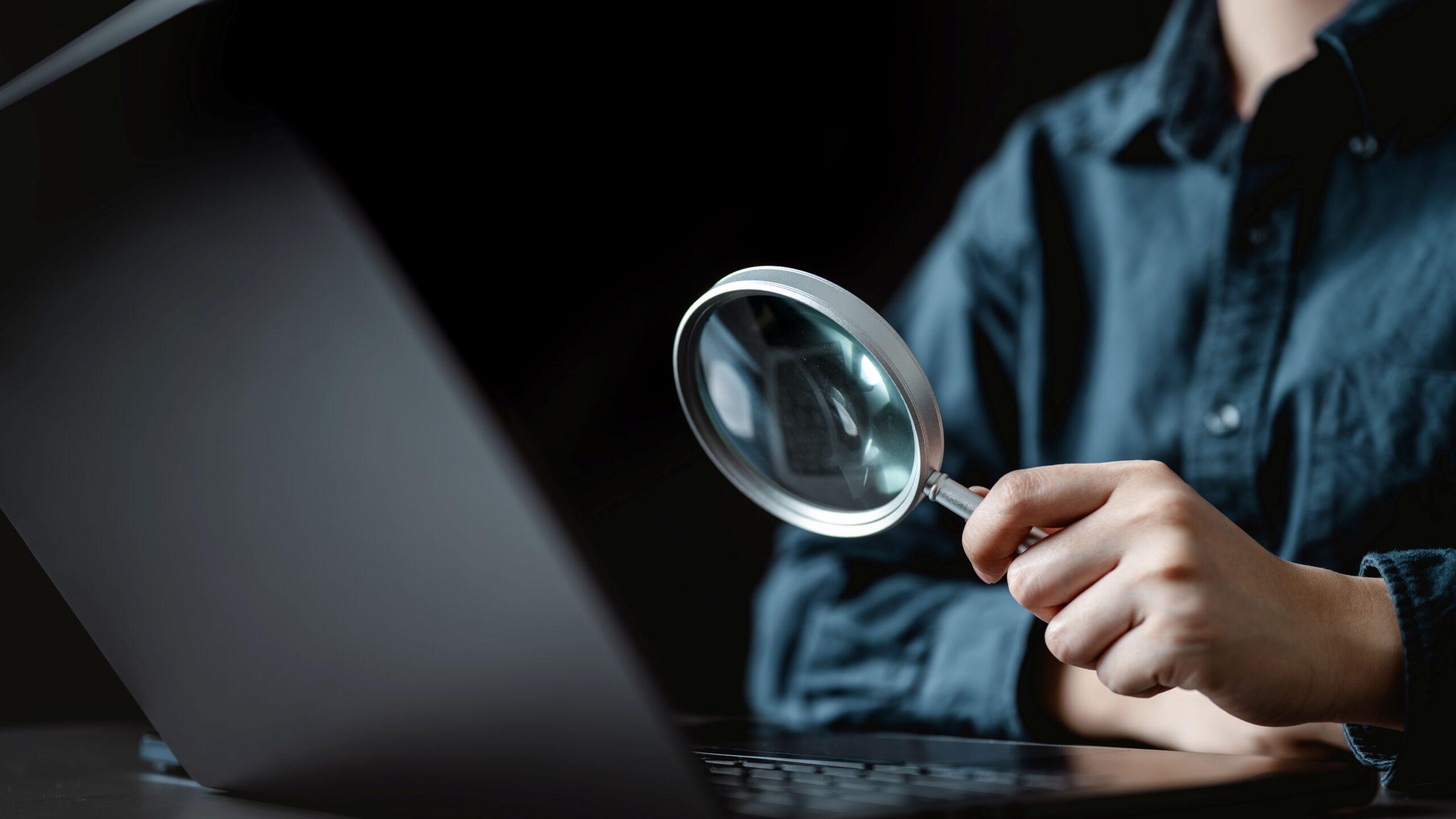 Person hält eine Lupe vor dem Laptop, als Symbol für klare Entscheidungen und sorgfältige Auswahl beim Schreckschusswaffen kaufen